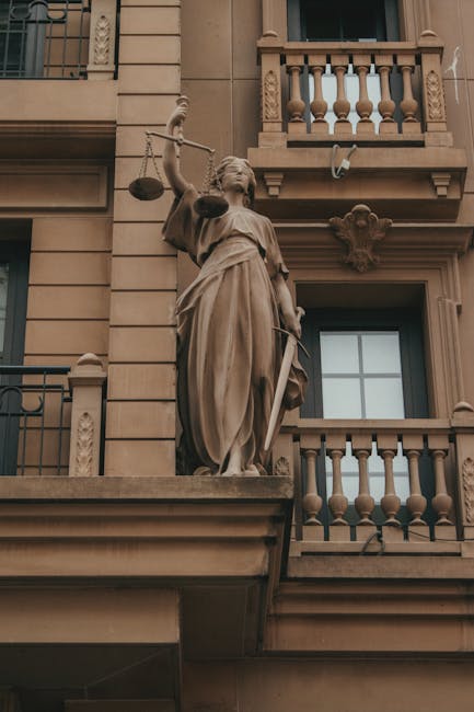 Elegante estatua de la Justicia con balanza y espada en la fachada de un edificio clásico, que simboliza la ley y la equidad.