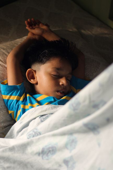 Un niño con una camisa de rayas duerme pacíficamente en el interior en un día soleado.