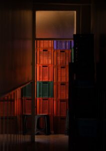Cajas de plástico naranjas y moradas apiladas en un almacén oscuro con una iluminación dramática.
