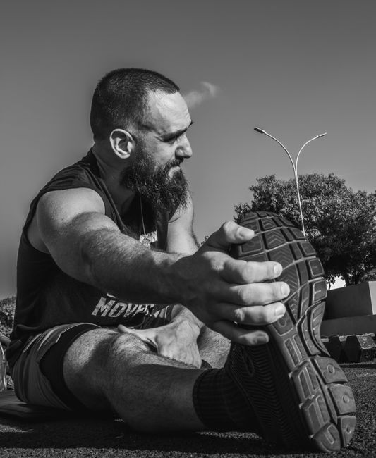 Hombre estirándose al aire libre en blanco y negro, mostrando motivación para hacer ejercicio.