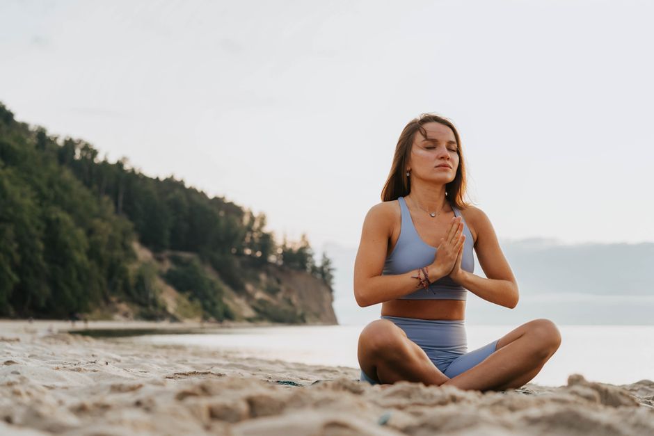 Mujer practicando meditación yoga en una playa serena por la mañana, promoviendo el bienestar.