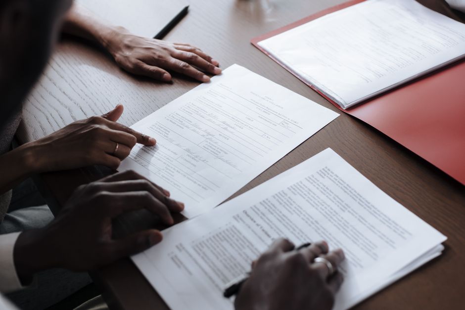 Dos individuos revisando y firmando documentos oficiales en un entorno interior.