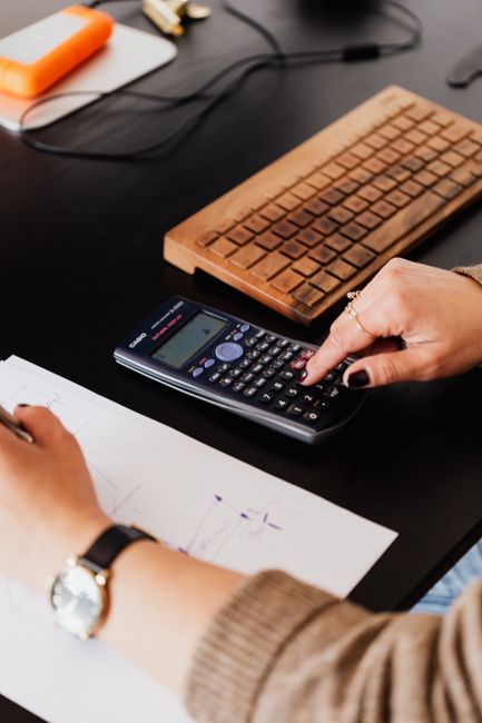Profesional de negocios utilizando una calculadora en un escritorio, rodeado de documentos.