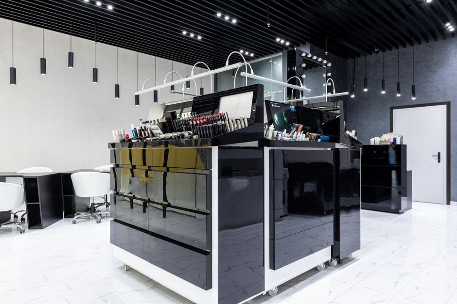 Interior elegante de tienda de maquillaje con gabinetes negros brillantes, sillas y abundante iluminación.