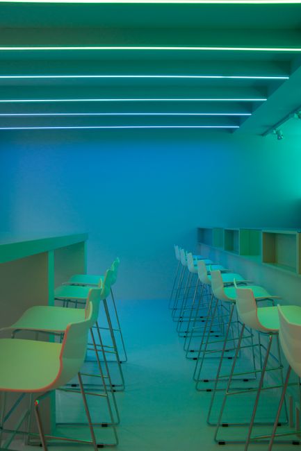 Un interior de bar minimalista elegante con iluminación de neón azul y verde y taburetes alineados.