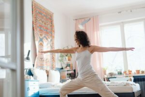 Una mujer practicando yoga en un dormitorio brillante y acogedor, creando una atmósfera serena y pacífica.