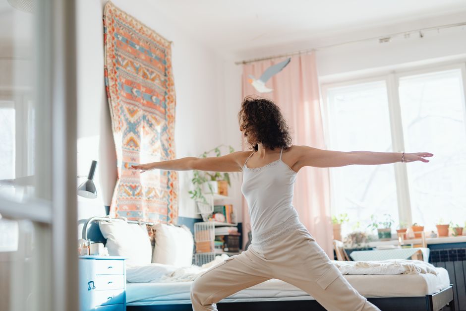 Una mujer practicando yoga en un dormitorio brillante y acogedor, creando una atmósfera serena y pacífica.