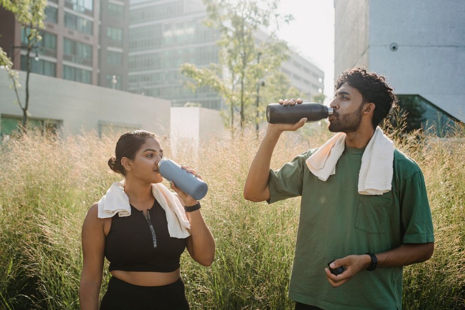 Un hombre y una mujer hacen una pausa refrescante, bebiendo agua después de ejercitarse en un parque urbano.