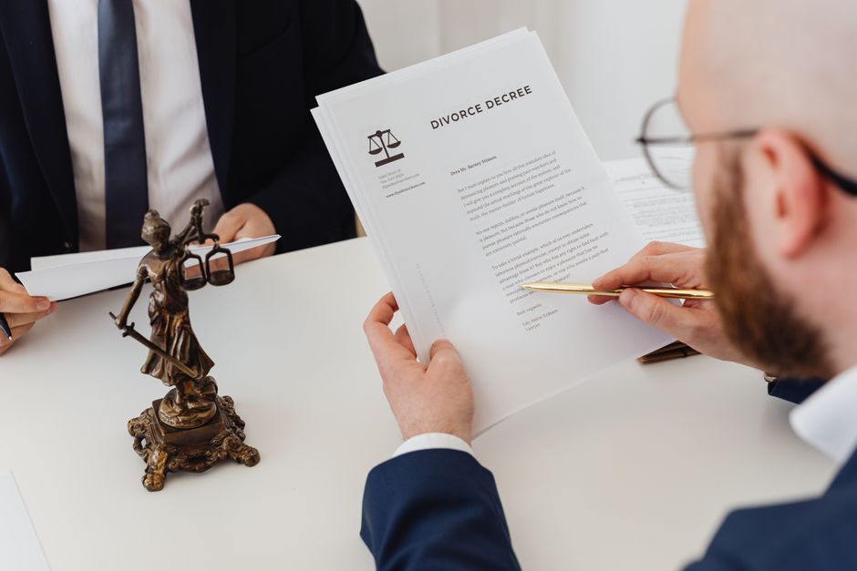 Dos profesionales examinando un decreto de divorcio con una estatua de la Justicia cerca.