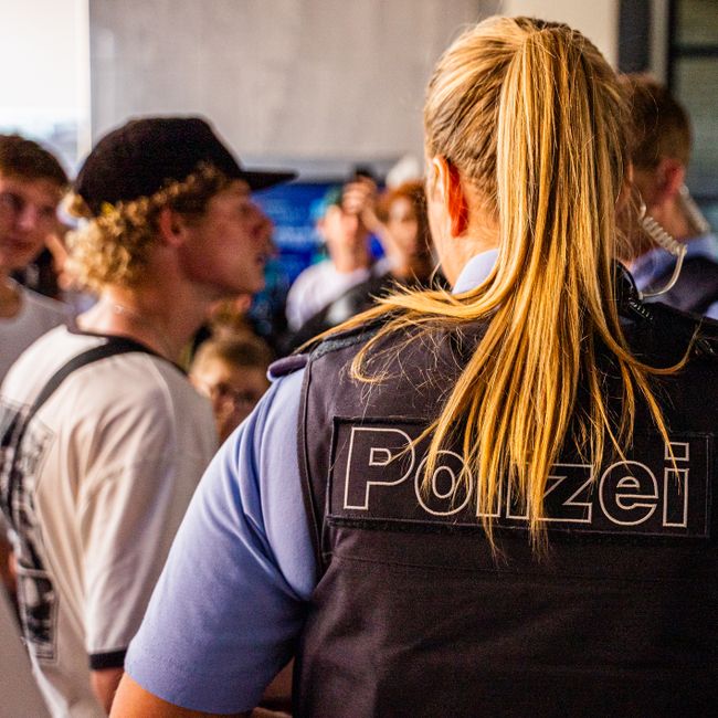 Una policía interactúa con un grupo de jóvenes en interiores, proporcionando seguridad y asistencia.